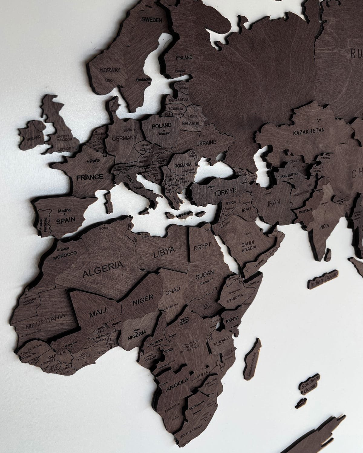 Drewniana mapa świata 3D w kolorze czekolady zawieszona na białej ścianie.